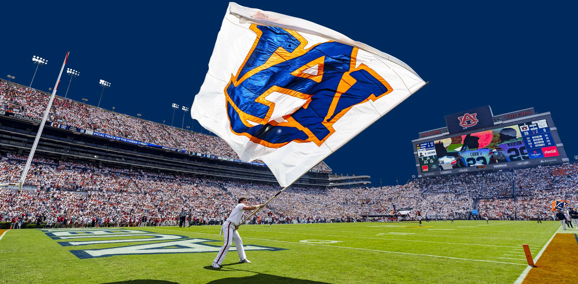 man waving a 'UA' flag on the football field